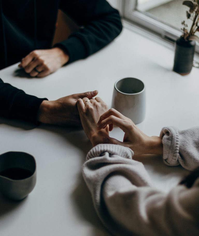 Händchenhaltendes Paar Zwei Personen halten Hände über einem Tisch auf dem zwei Tassen und eine kleine Pflanze stehen